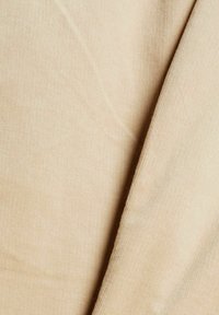 Tissu en velours côtelé beige avec des côtes verticales visibles et un pli créant une ombre sur le côté droit.