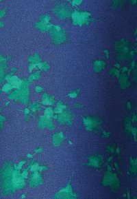 Tissu bleu avec une surface texturée et un motif de grappes de feuilles vertes éparpillées.