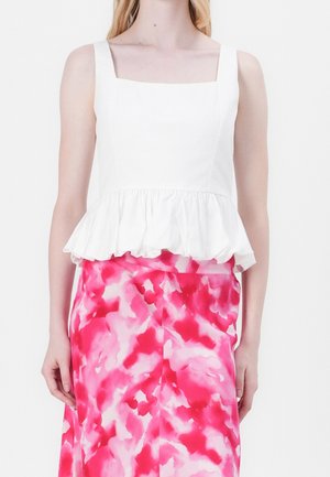 Kobieta w białej, bezrękawnikowej bluzce typu peplum w połączeniu z różowo-białą spódnicą w abstrakcyjny wzór.