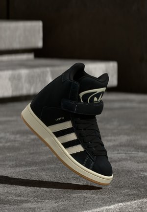 Sneakers alte nere con tomaia in suede, design a tre strisce bianche, suola strutturata e cinturino regolabile. Dotate di colletto e linguetta imbottiti.