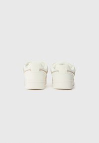 White sneakers with a smooth texture, featuring a rounded shape, subtle beige accents, and cushioned heel support. Minimalistic design.