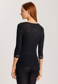 Top lungo aderente nero con inserti in pizzo alle maniche a tre quarti. Tessuto rigato e scollatura a barca. Leggera trasparenza.