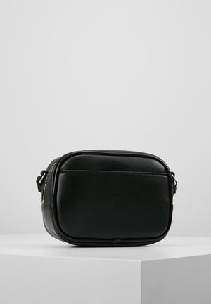 Kompaktowa czarna torebka na ramię z zaokrąglonymi krawędziami i srebrnym zamkiem błyskawicznym, spoczywająca na białym piedestale na tle jednolitego szarego tła.