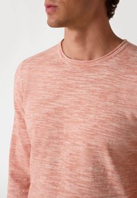 Cămașă lungă cu mâneci lungi, de culoare coral deschis, realizată dintr-un material moale, texturat, cu decolteu rotund și un model subtil.