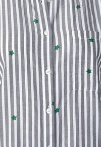 Camicia a righe bianca e grigia in tessuto con ricamo di stelle verdi, dotata di taschino sul petto e bottoni tondi in plastica.