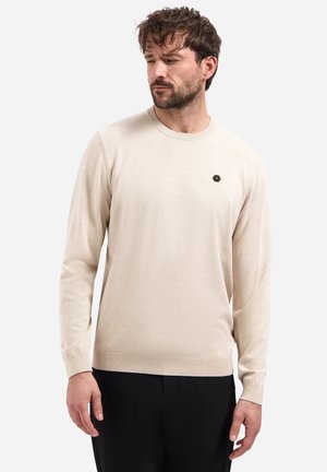 Beige trui met een ronde hals, lange mouwen en geribbelde boorden. Voorzien van een klein zwart zeshoekig logo op de borst. Zachte textuur.