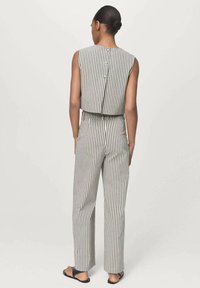 Gestreifter Jumpsuit mit taillierter Passform, ärmellosem Design und Knopfdetails hinten. Hergestellt aus leichtem Material in einer neutralen Farbpalette.