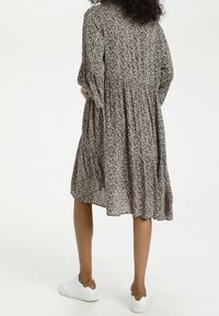 Blumenkleid mit dunklem grünen Hintergrund und kleinen rosa und weißen Blumenmustern, gerafftem Taillenbereich und Ärmeln bis zum Ellenbogen.