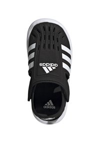 Svart slip-on sko med teksturert overflate, tre hvite striper og forsterket hæl. Har perforeringer for ventilasjon og merket logo.