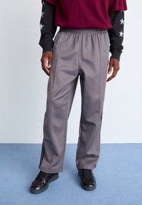 Grå treningsbukser med en avslappet passform, smale ben og elastisk midje. Kombinert med en burgunder oversized topp og svarte sneakers.