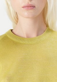 Maglione giallo in maglia con collo rotondo a coste e una texture leggera. Vista ravvicinata che mette in evidenza la fine trama del tessuto.