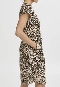 Klänning i leopardmönster med korta ärmar, elastisk midja och sidofickor. Tillverkad av lättviktig tyg, med bruna, svarta och krämfärgade nyanser.