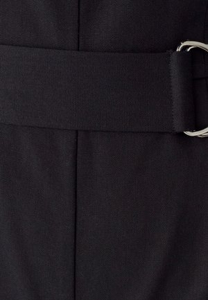 Gros plan sur une ceinture en tissu noir avec une boucle à double anneau en argent sur un vêtement texturé assorti.