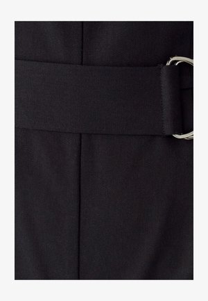 Primer plano de un cinturón de tela oscura con una hebilla de doble anillo plateada sobre una prenda texturizada a juego.