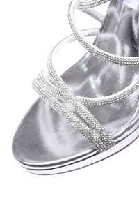 Sandalo argentato con tacco alto, caratterizzato da molteplici cinturini scintillanti, una suola liscia e lucida, e un design elegante con punta aperta.