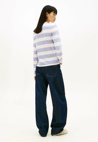 Camisa de manga larga a rayas en azul claro y blanco combinada con unos vaqueros de pierna ancha azul oscuro, con costuras visibles y bolsillos.