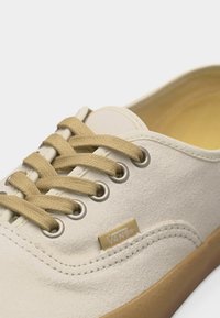 Λευκό σουέντ αθλητικό παπούτσι Vans με μπεζ κορδόνια, μεταλλικά οπές και σόλα από καουτσούκ χρώματος τσίχλας, εμφανίζεται σε κοντινό πλάνο.