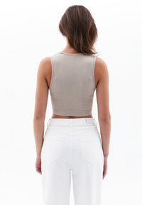 Top corto beige con una texture a coste e design senza maniche, abbinato a jeans in denim bianchi a vita alta.