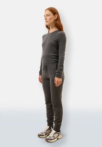 Szary zestaw dresowy z dzianiny, składający się z długiego rękawa i spodni z troczkami. Teksturowany materiał, dopasowany krój, w połączeniu z szarymi i beżowymi sneakersami.