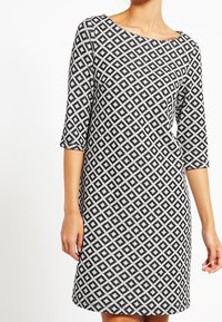 Abito bianco e nero con motivo a rombi, maniche a tre quarti, scollo rotondo e una silhouette leggermente svasata. Tessuto dalla texture liscia.