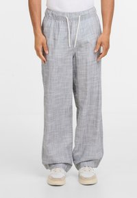 Světlé šedé kostkované široké kalhoty vyrobené z měkkého materiálu. Mají stahovací pas a jsou doplněny bílými teniskami.