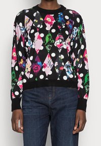 Sort sweater med diamantmønster og farverige blomsterprints samt prikker. Ribbede manschetter og kant. Båret med mørkeblå jeans.