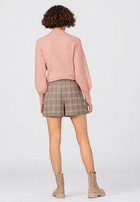Pull court rose avec des manches ballons, associé à un short à carreaux dans des tons beige et marron, et des bottines à talon épais couleur tan.