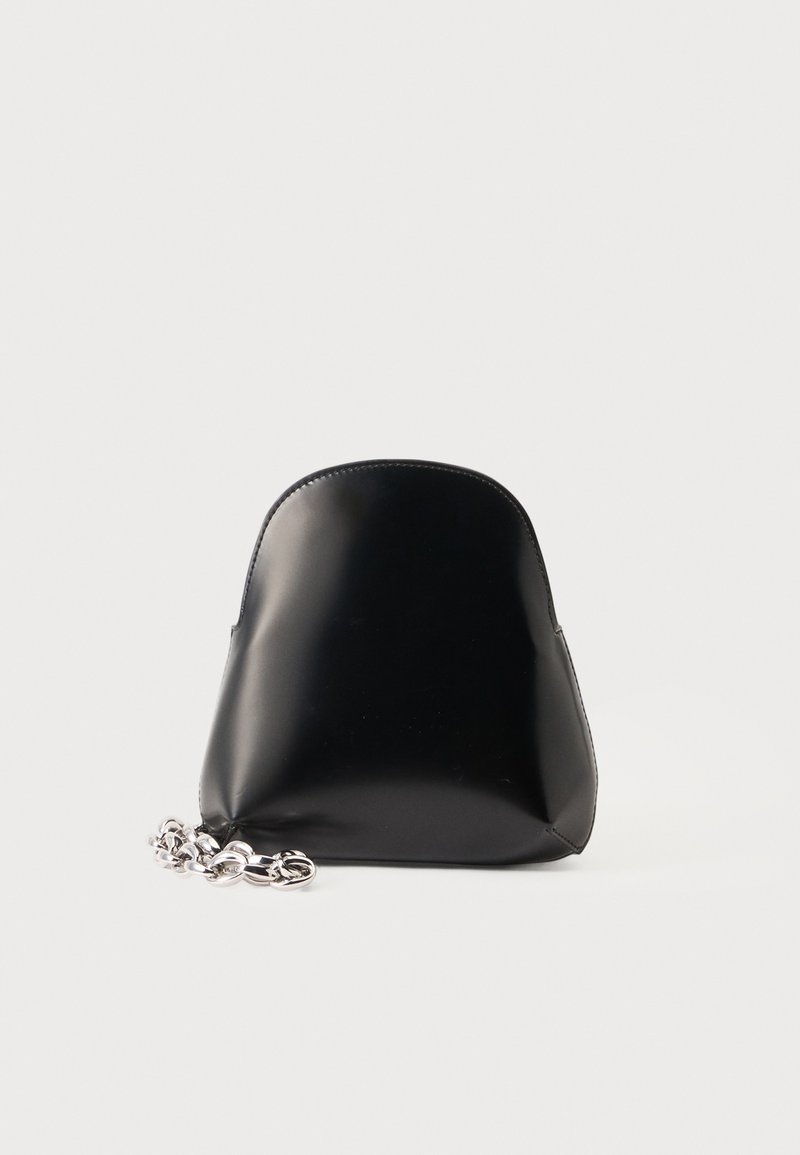 Petit sac à main en cuir noir avec un dessus arrondi et une bandoulière chaîne argentée posée à côté sur un fond blanc uni.