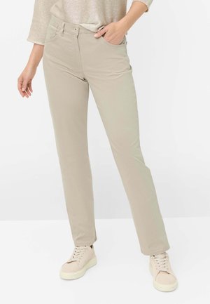 Femme portant un pantalon beige droit avec poches avant, associé à des baskets beige clair et un pull léger en maille.