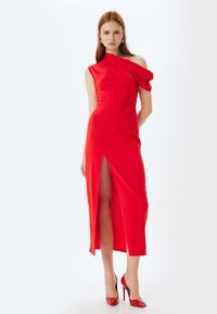 Vestido rojo asimétrico con una silueta ajustada, que presenta una abertura en el lado izquierdo, textura suave y un diseño de un solo hombro.