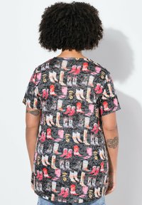 Camiseta de manga corta con un tejido negro y un patrón colorido de varios botas y zapatos, presentado en un diseño repetido.