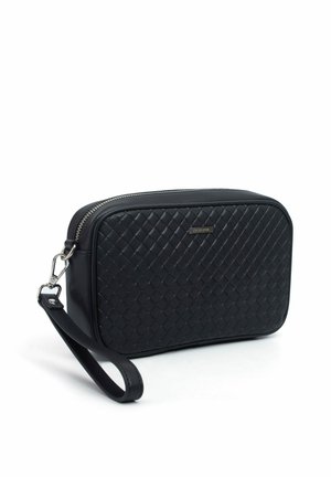 Hand houdt een zwarte woven leren clutch met een zilveren ritssluiting vast tegen een witte achtergrond.