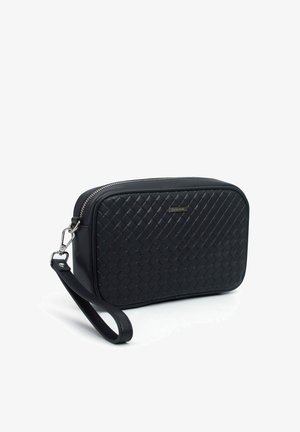 Hand houdt een zwarte woven leren clutch met een zilveren ritssluiting vast tegen een witte achtergrond.
