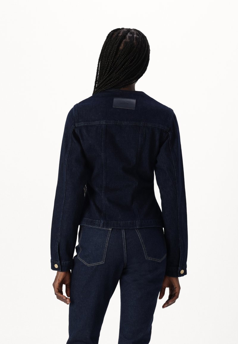 Veste en jean foncé avec une coupe ajustée, des manches longues et une étiquette en cuir au dos. Détails de coutures contrastées et poignets à bouton.