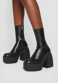 Zwarte leren enkellaarzen met een hoge plateauzool en stevige hak. Voorzien van een zijrits en een gladde textuur, met een naadloos ontwerp.
