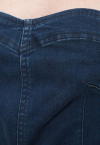 Σκούρο τζιν ύφασμα με κοντινό πλάνο στη ραφή στην πλάτη, με ορατές λεπτομέρειες ραφής και ελαφρώς ξεθωριασμένη υφή.