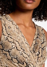 Robe à imprimé serpent beige et noir avec décolleté en V et design enveloppant, présentant une texture douce et un léger brillant. Accentuée de détails subtils.