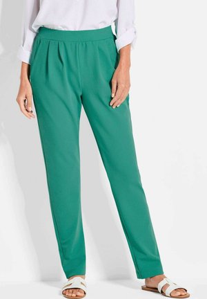 Pantalons plissés verts en tissu doux, dotés d'une taille plate et d'un design de jambe fuselée. Associés à des sandales blanches.