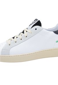 White leather sneaker with textured grey accents, cream laces, and a rubber sole. Features black detailing on the heels and side branding.