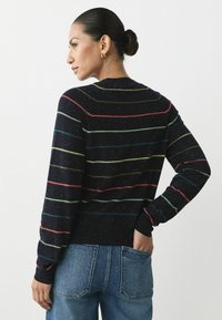 Sort sweater med multikolorede vandrette striber, der har en struktureret finish. Designet inkluderer en rund halsudskæring og ribkanter.