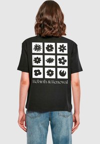Tricou din bumbac negru cu un grilaj de nouă desene florale negre pe spate, cu textul "Rebirth & Renewal" dedesubt.
