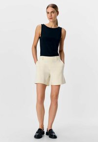 Zwarte mouwloze top gecombineerd met lichtbeige shorts. De outfit heeft een minimalistisch ontwerp met een gladde textuur en geen zichtbare patronen.