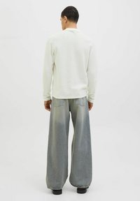 White pullover with a textured fabric and long sleeves, paired with wide-leg faded gray jeans and black shoes. Viewed from the back.