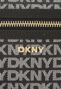 Juodos ir baltos spalvų raštų rankinė su auksiniu užtrauktuku, ant tekstūruoto paviršiaus išryškintai pateikiamas DKNY logotipas, taip pat aukso spalvos.