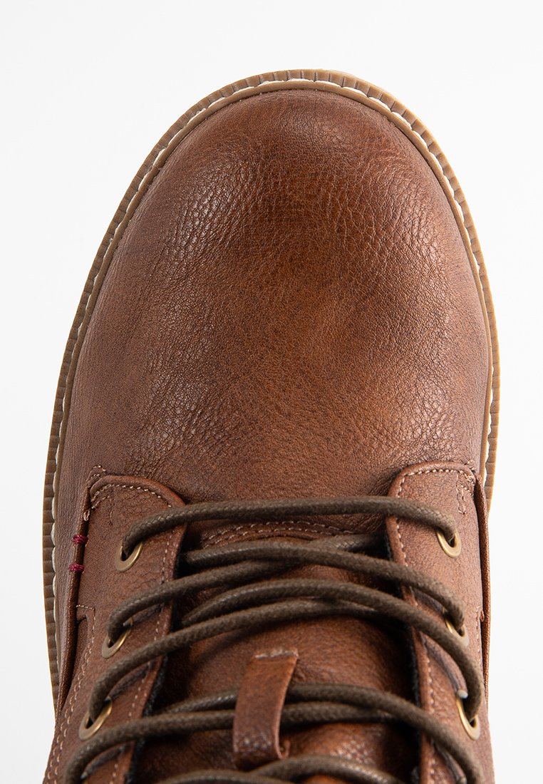 Close-up of brown leather lace-up boot with textured surface and light brown stitched sole edge against white background.