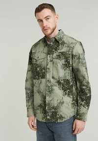 Grön digital kamouflage skjorta med knappar, två bröstfickor, spread collar och en strukturerad tyg. Har en liten logotyp på vänstra fickan.