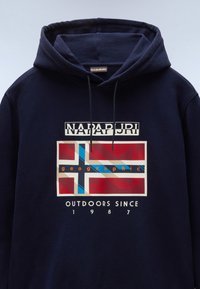 Marineblauwe Hoodie met een grafisch ontwerp aan de voorkant, featuring een gestileerde vlag in rood, blauw en crème, met de tekst "NAPAPIJRI geographic" en "OUTDOORS SINCE 1987."