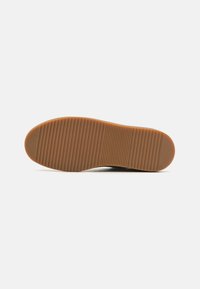 Rubber shoe sole, tan color with horizontal grooves for traction. Rounded toe, slightly raised heel, smooth edge profile.