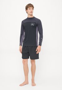 Czarna koszulka typu rashguard z długim rękawem, z szarymi panelami bocznymi i logo na froncie, w zestawie z czarnymi szortami do pływania z teksturowanym wzorem.