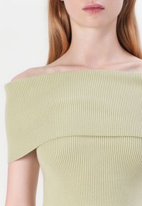 Top de canalé sin mangas en verde claro, con un diseño de punto texturizado y un escote amplio que enmarca elegantemente los hombros.